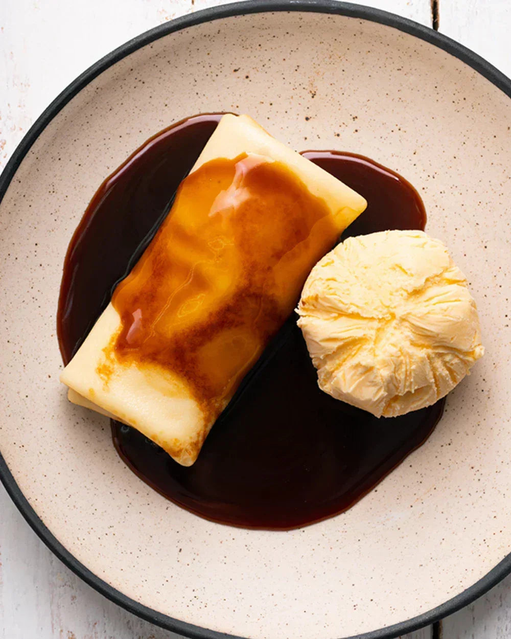 Banana crepe with coconut caramel sauce and vanilla ice cream on a speckled plate