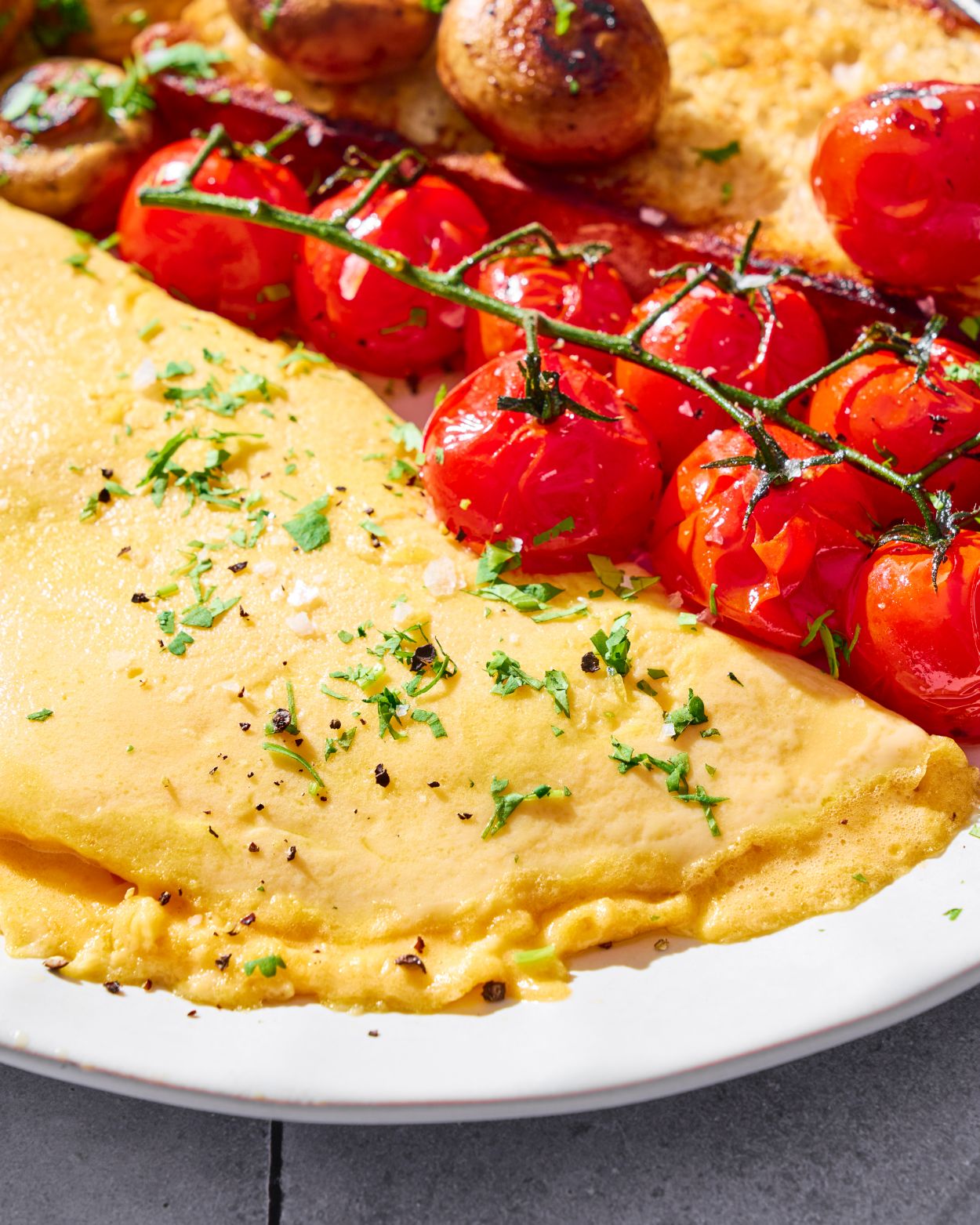 Fresh omelette garnished with herbs, served with roasted cherry tomatoes and mushrooms on a plate