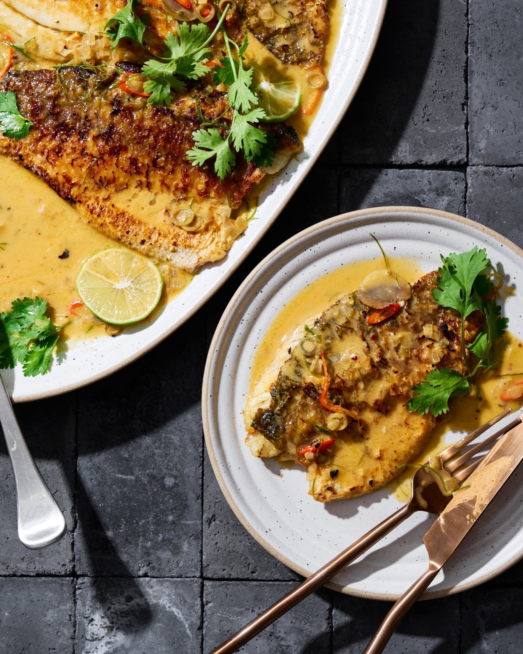 Seared fish fillet in yellow curry sauce, garnished with cilantro, lime, and sliced chilies on ceramic plates.