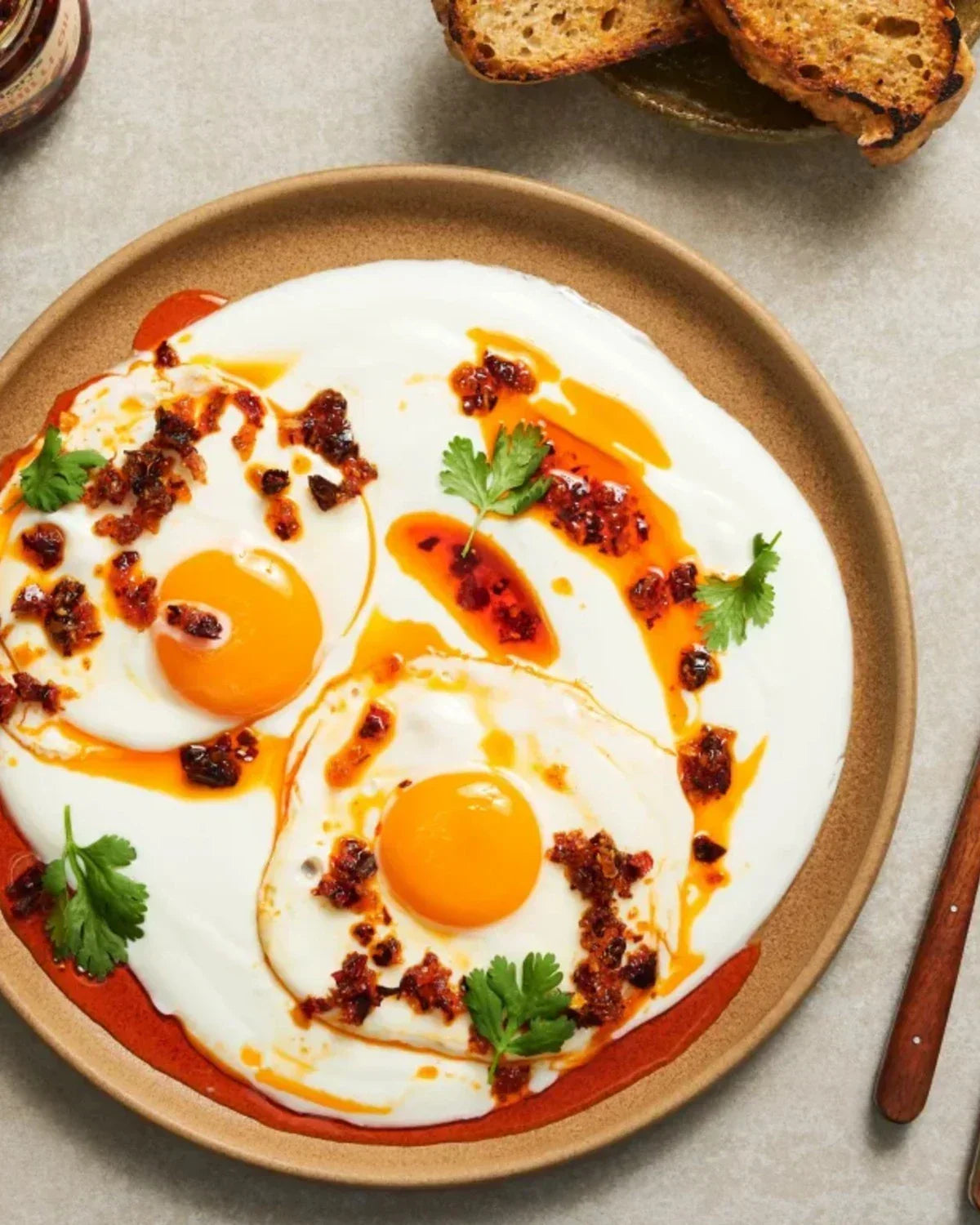 Fried eggs on yogurt topped with chili crisp oil and cilantro, served with toasted bread