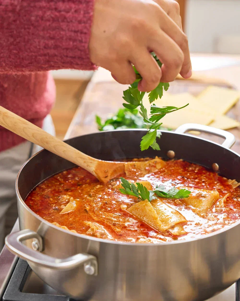 Hand garnishing lasagna soup in stainless steel pot with fresh parsley