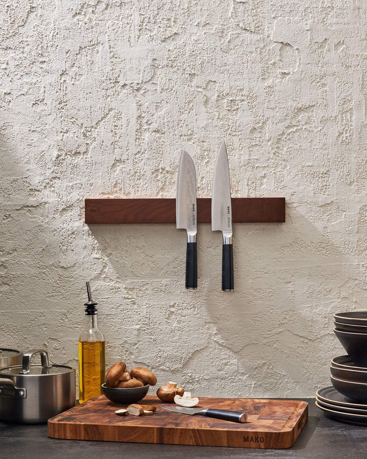 Kitchen scene with two chef knives on a magnetic strip, cutting board, mushrooms, cookware.