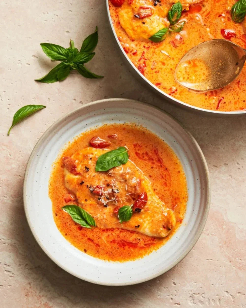Creamy chicken breast in tomato sauce with fresh basil leaves on a plate, top view