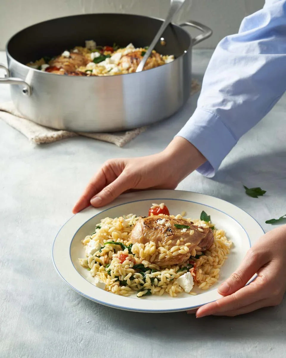 One-pot chicken and orzo served on a plate with spinach and tomatoes beside a stainless steel pan.
