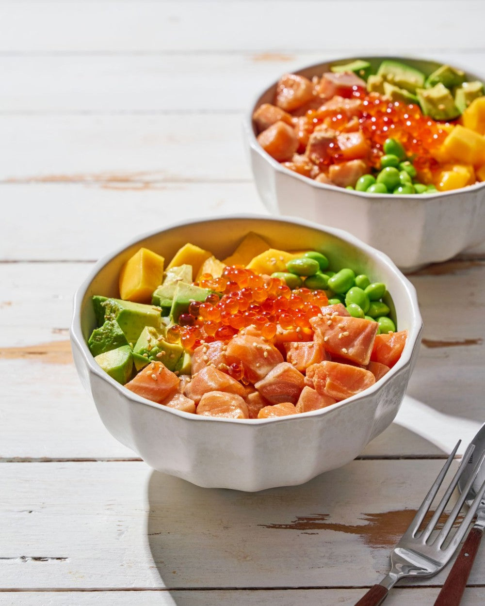 Salmon poke bowl with avocado, mango, edamame, and salmon roe on a white wooden table