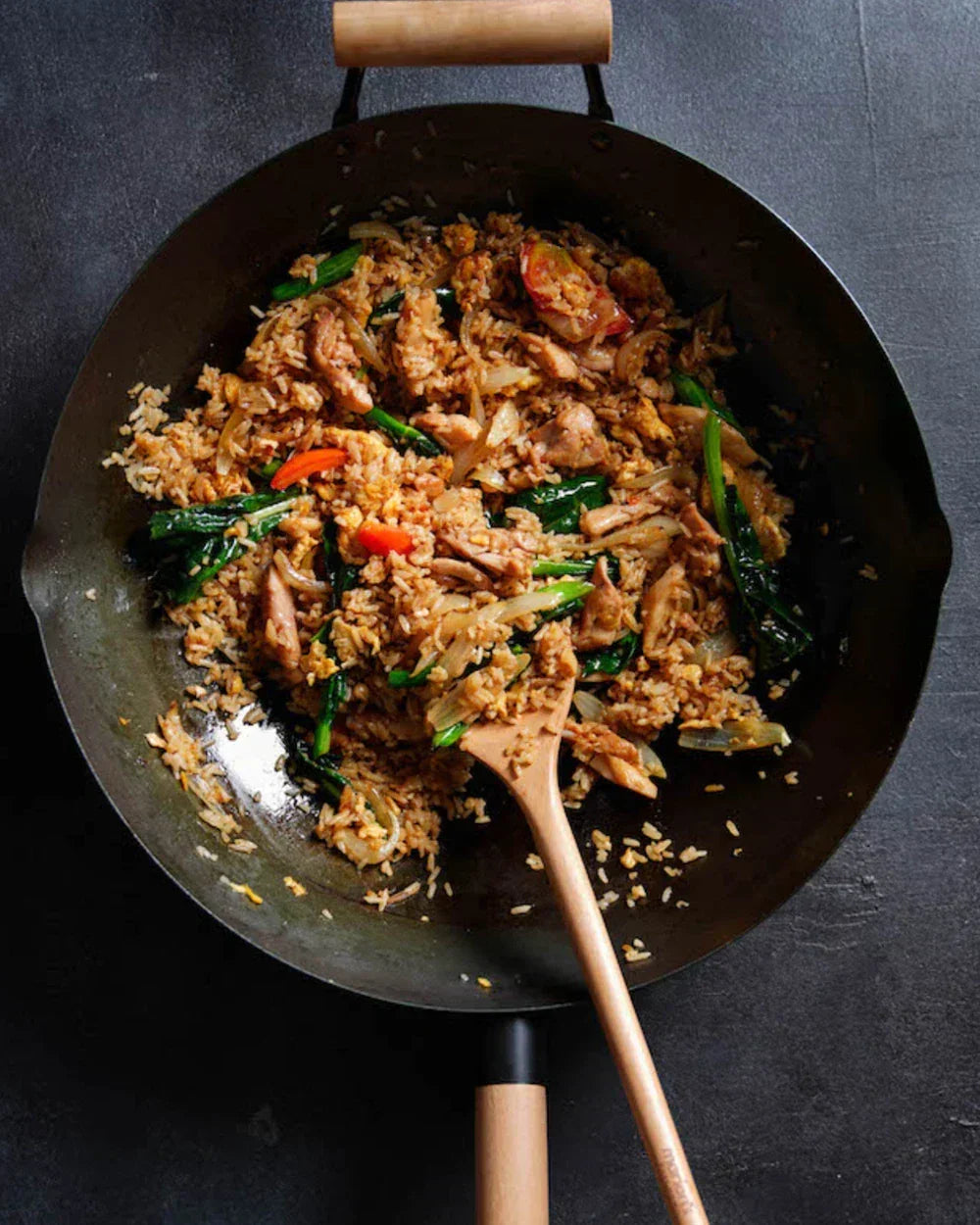 Thai chicken fried rice with vegetables in a wok, wooden spatula on dark background