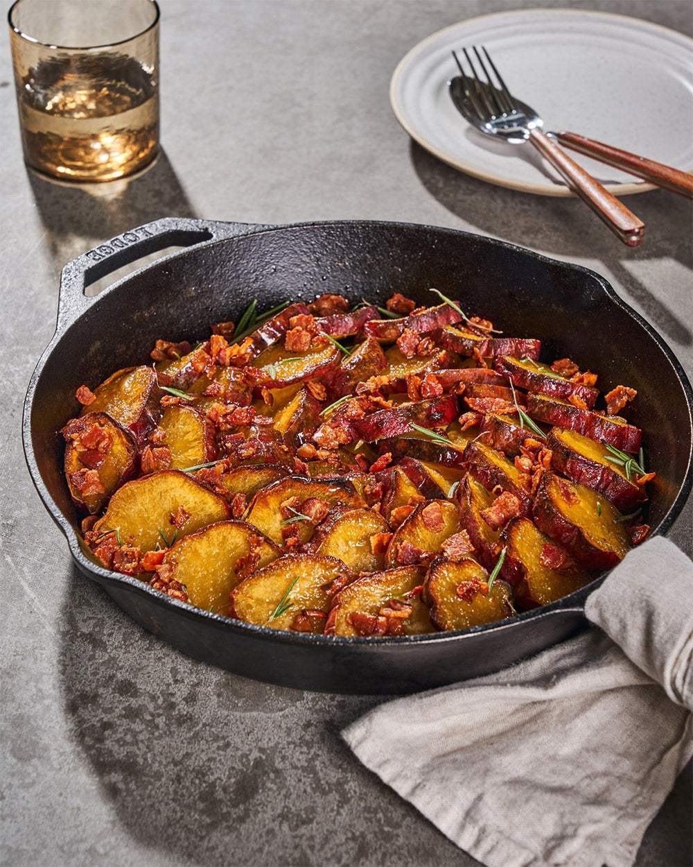 Roasted sweet potato slices with crispy bacon and herbs in a cast iron skillet