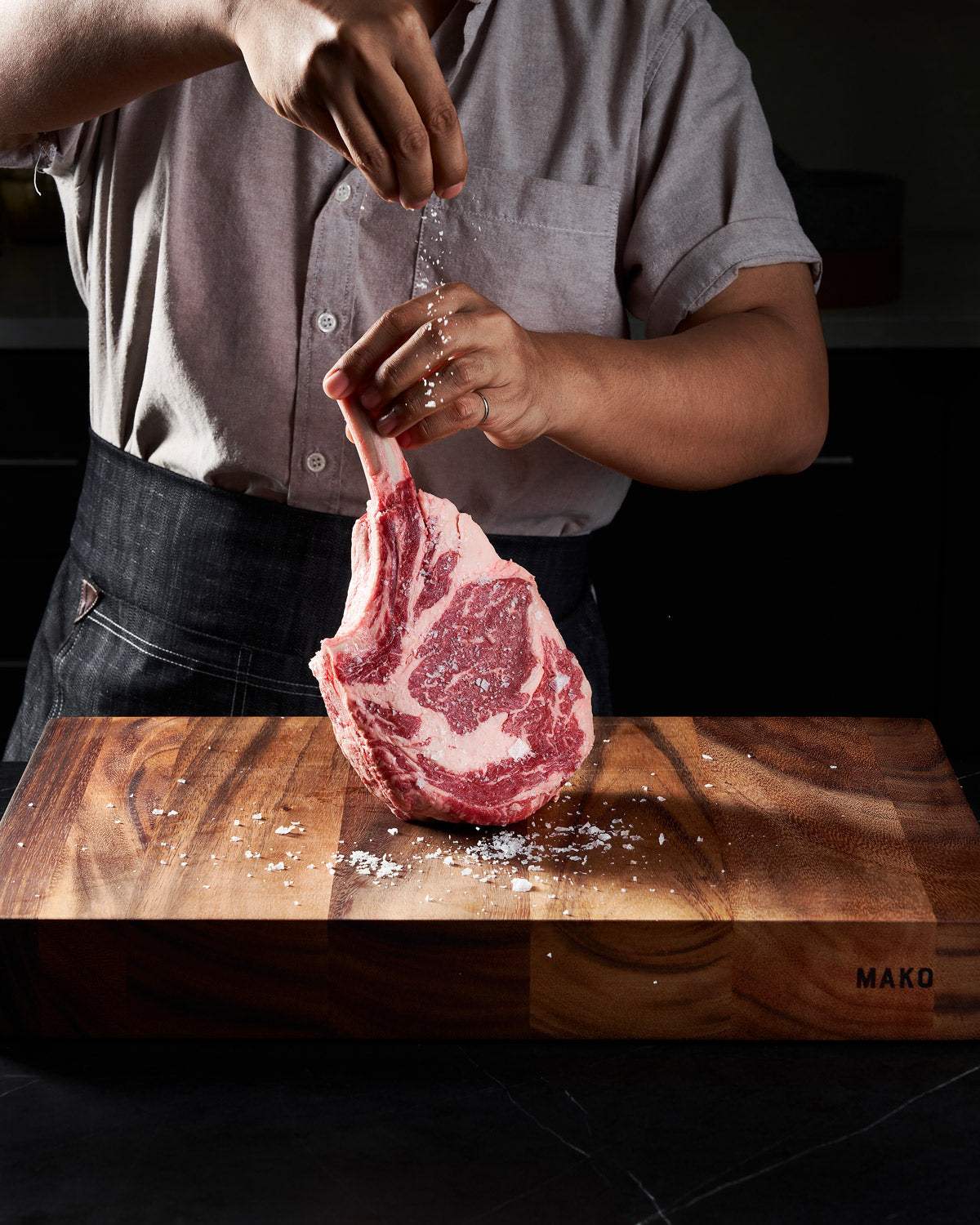 Hand seasoning raw tomahawk steak on a wooden chopping board in a kitchen setting