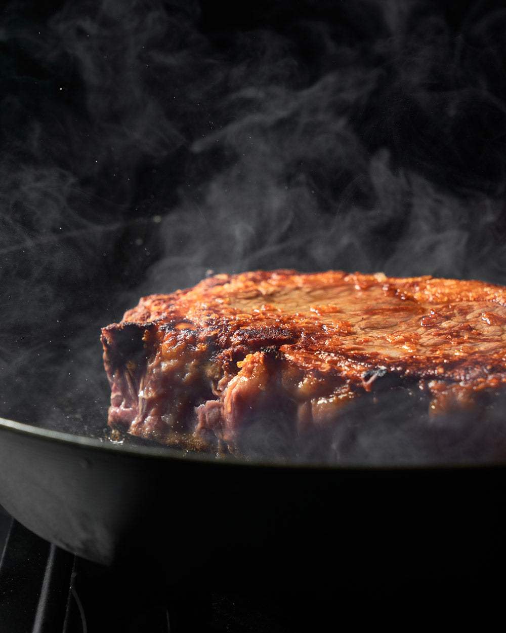 Juicy seared steak sizzling in a black skillet with rising steam