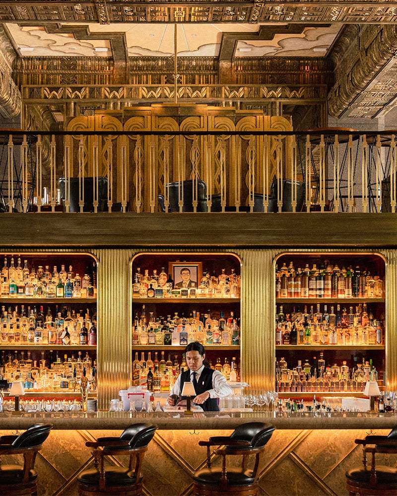 Elegant bar interior with shelves of liquor bottles, art deco design, and bartender preparing a drink