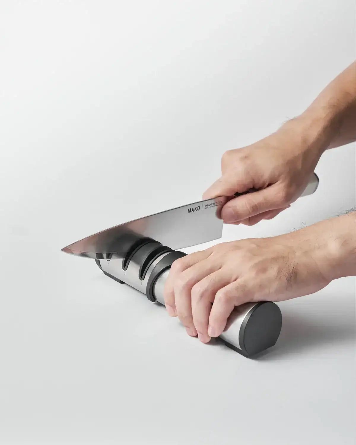 Hands sharpening a Mako Japanese steel knife on a three-stage metal knife sharpener