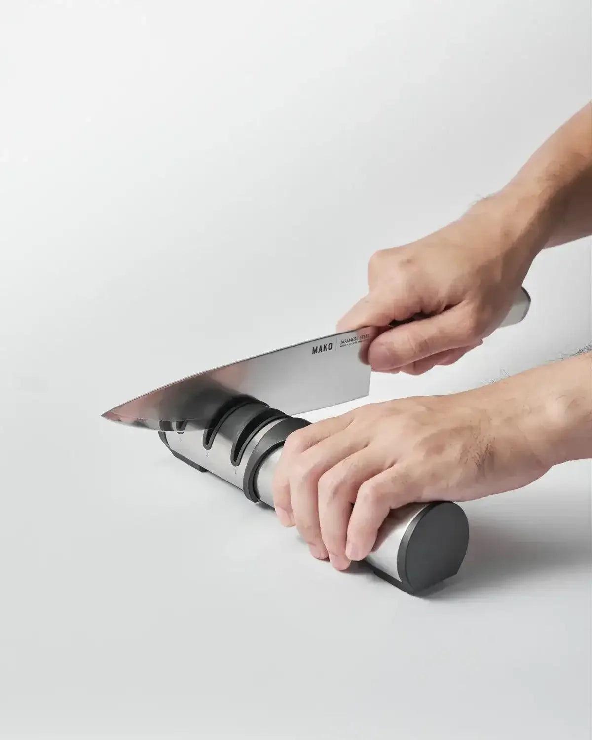 Hand using a stainless steel knife sharpener to sharpen a kitchen knife on a white surface.