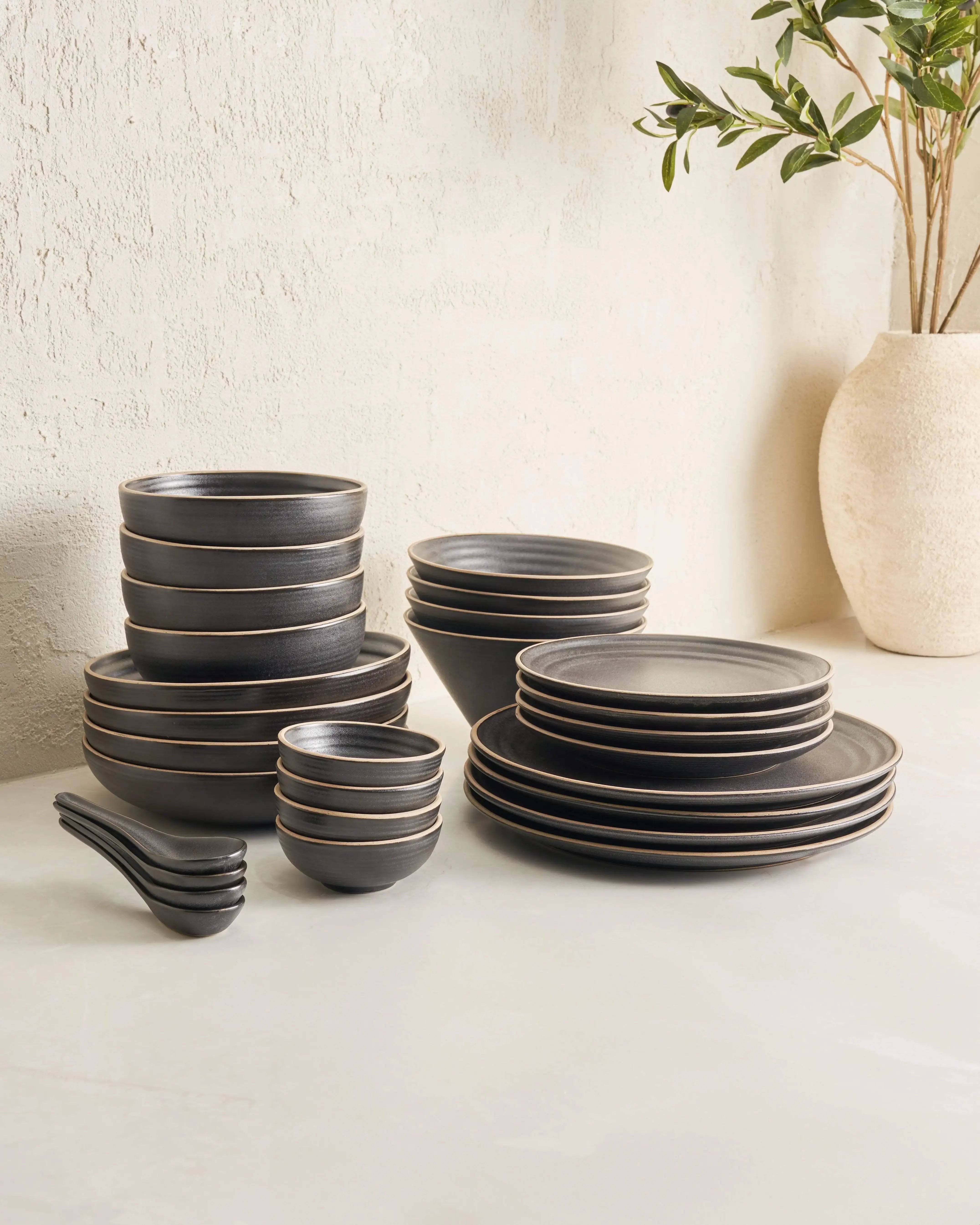 Asoke Charcoal complete dinnerware set by Marion Grasby with bowls, plates, and spoons on light surface