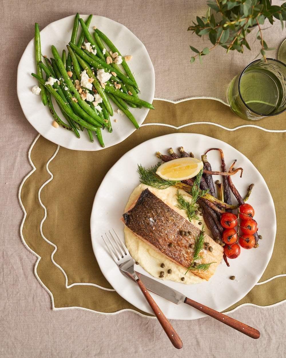 Grilled salmon with mashed potatoes, roasted carrots, cherry tomatoes, and green beans on ceramic plates