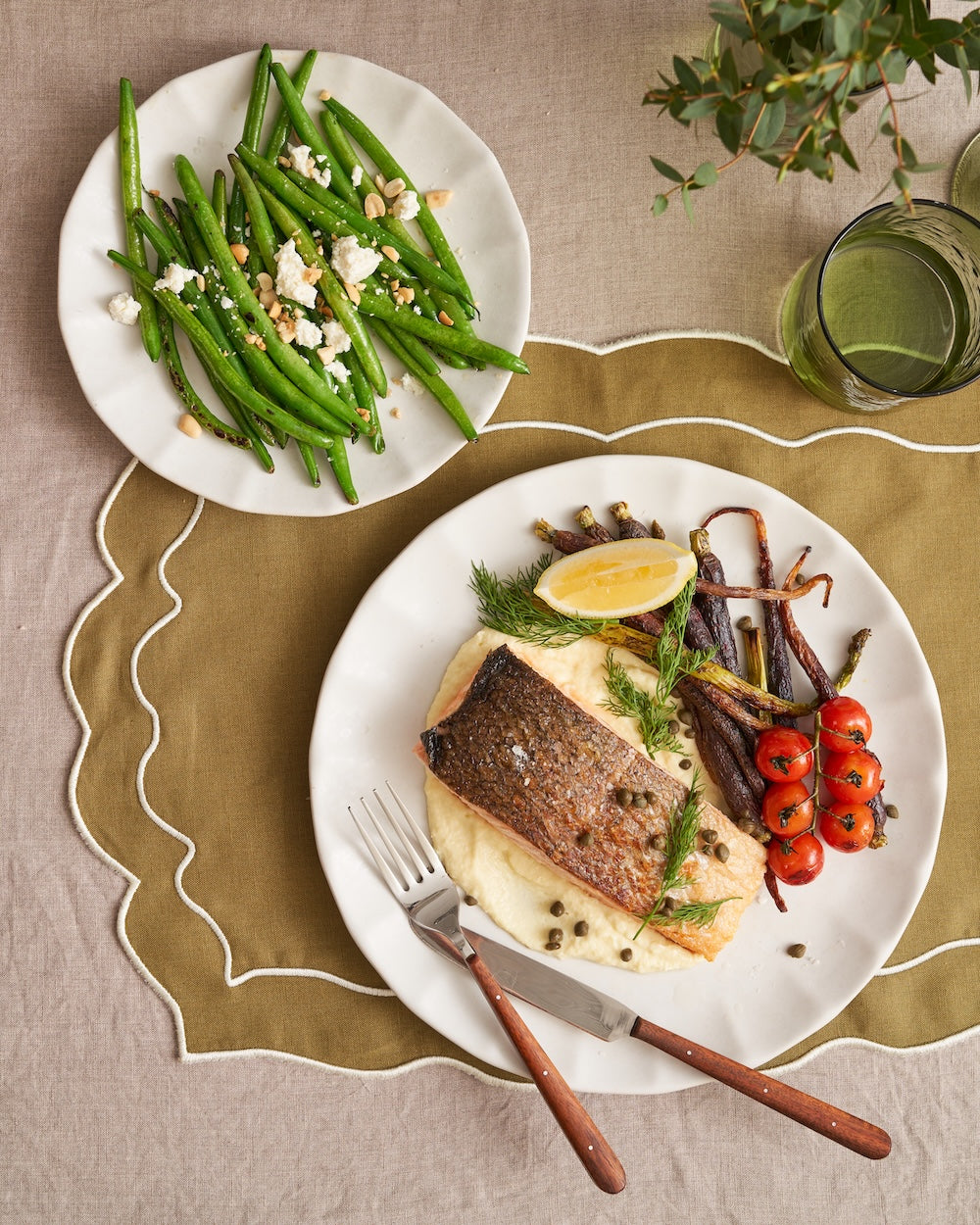 Grilled salmon on creamy mash with roasted carrots and tomatoes, green beans with feta, elegant table setting.