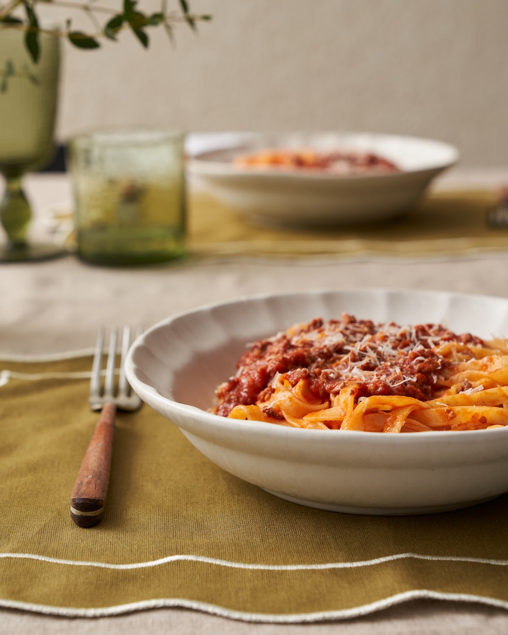 Ceramic bowl with pasta and tomato sauce on a table set with green glassware and a fork