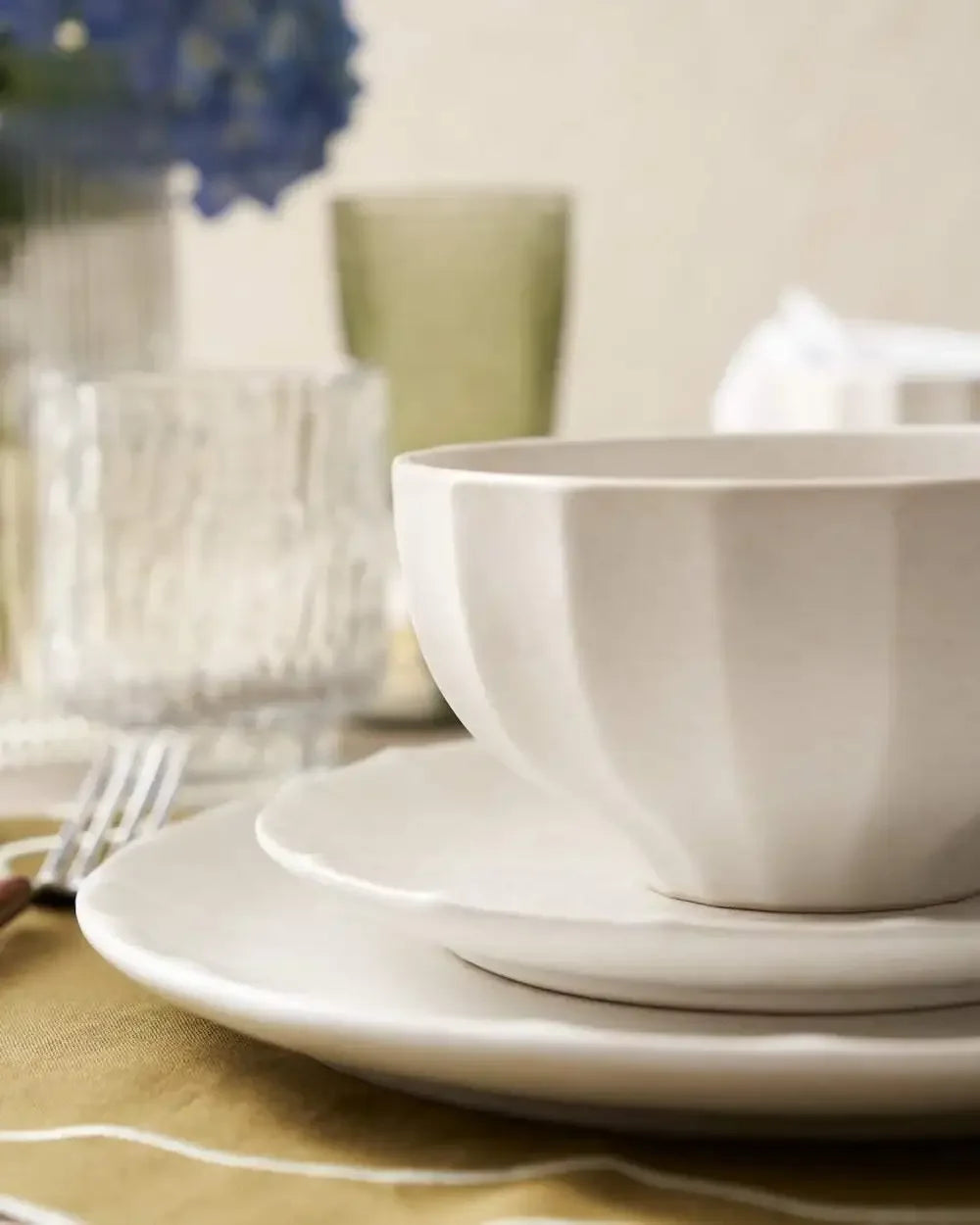 Neutral ceramic bowl and plates on a set dining table with glassware and cutlery.
