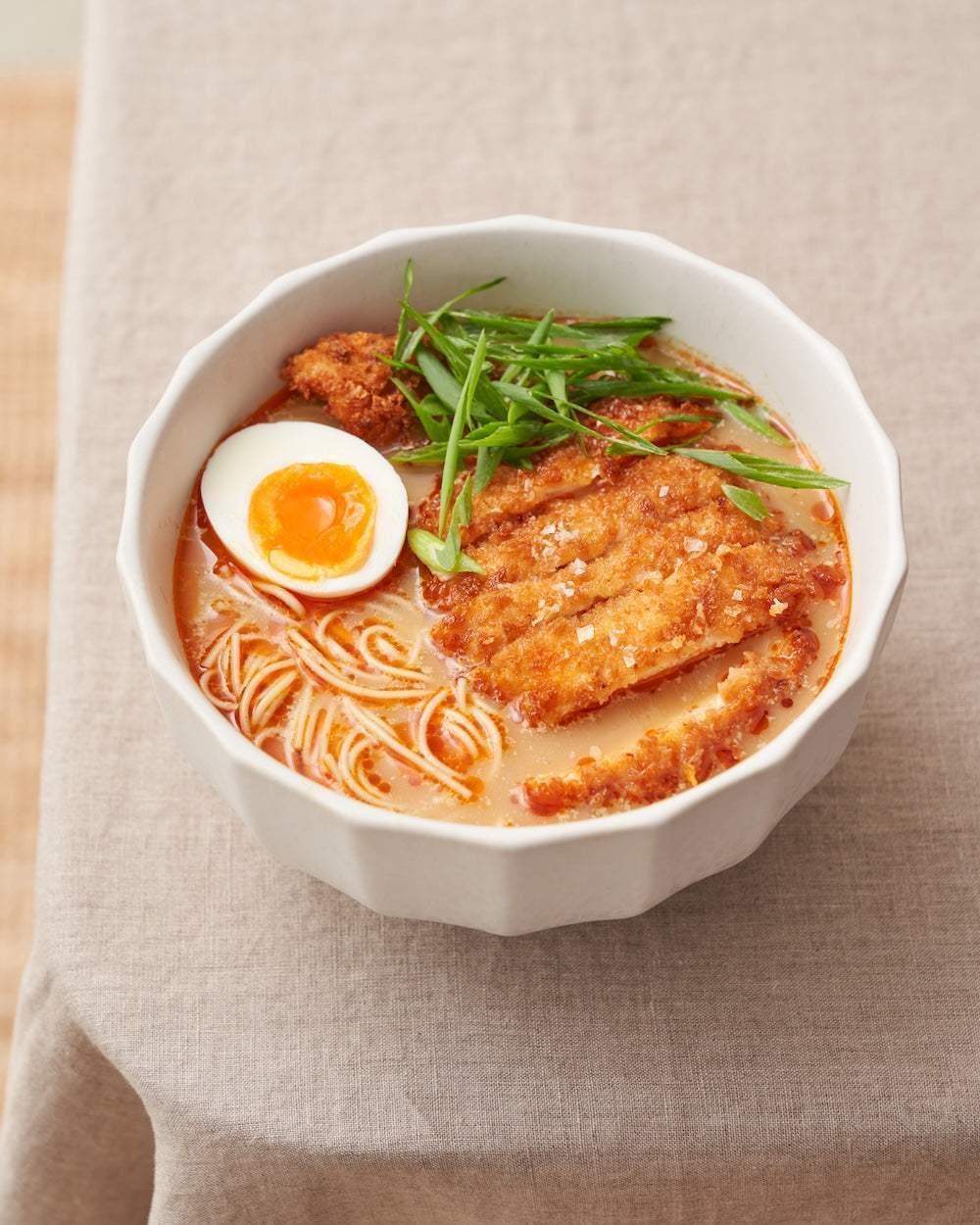 Asoke ceramic bowl with crispy fried chicken ramen, soft-boiled egg, and green onions on beige cloth