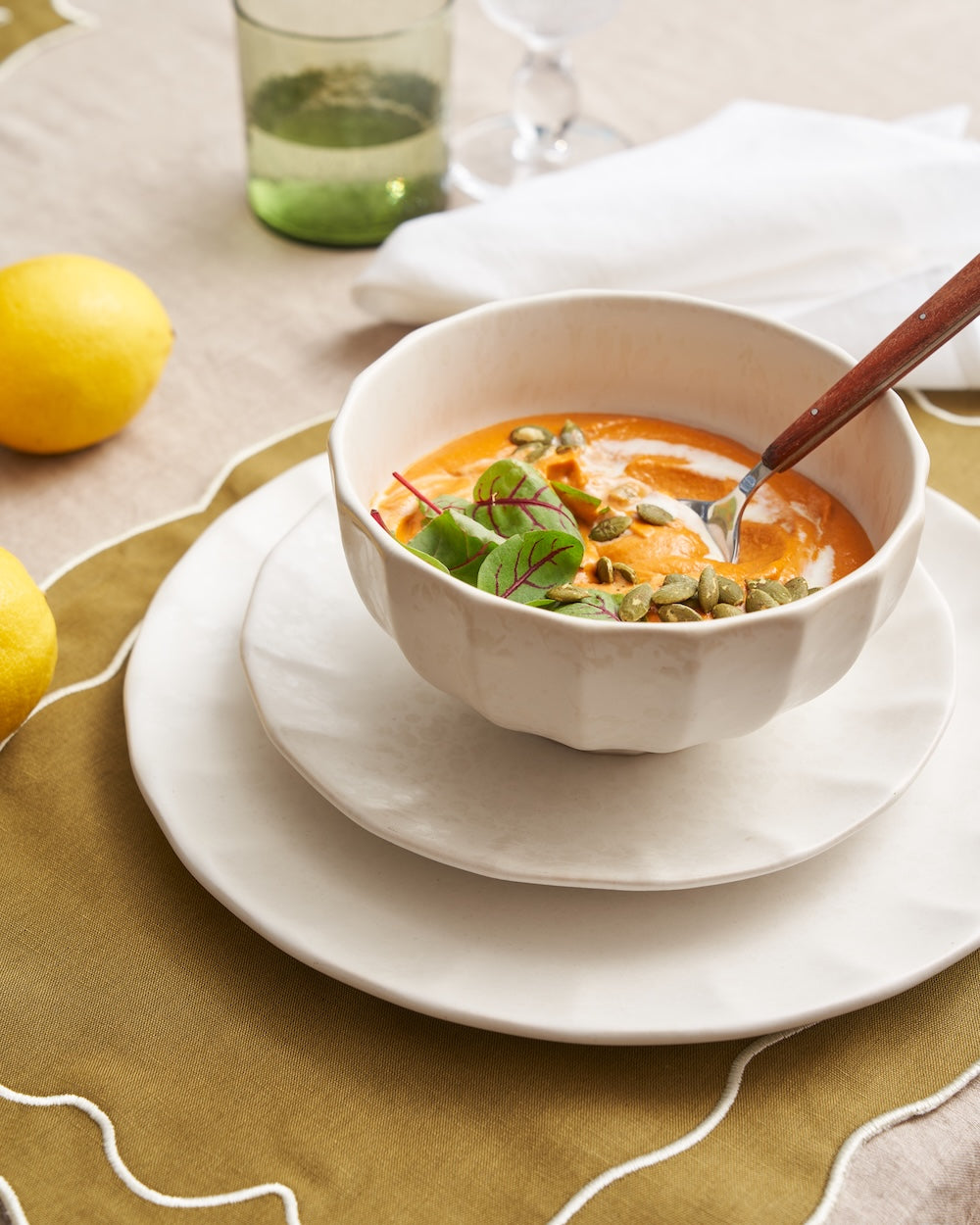 Creamy soup with seeds and greens in a handmade white ceramic bowl on a set table