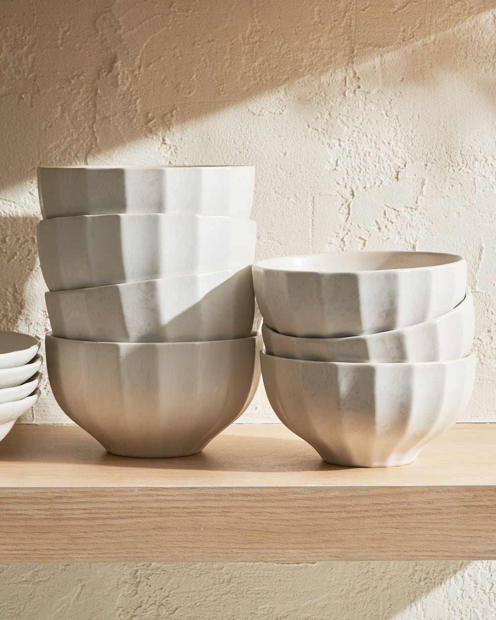 Stack of white ceramic bowls with ribbed texture on wooden kitchen shelf