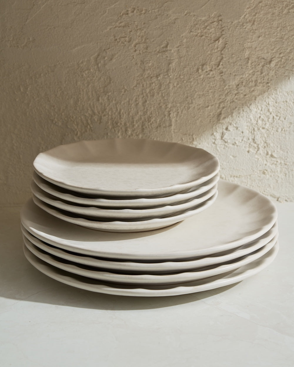 Stack of handmade cream ceramic dinner plates with organic edges on a textured surface