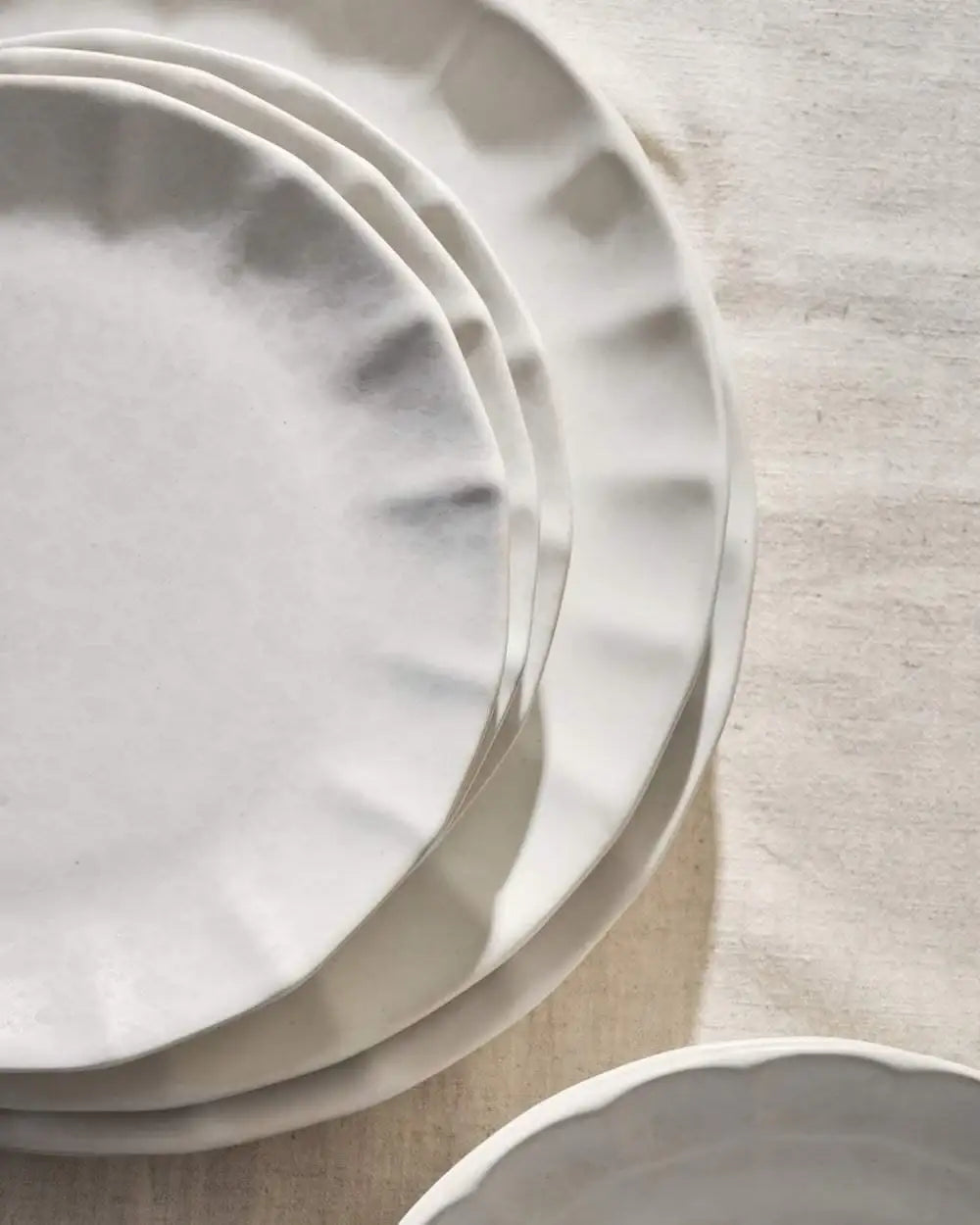 Stack of white, irregularly shaped ceramic plates with subtle texture on a light fabric surface