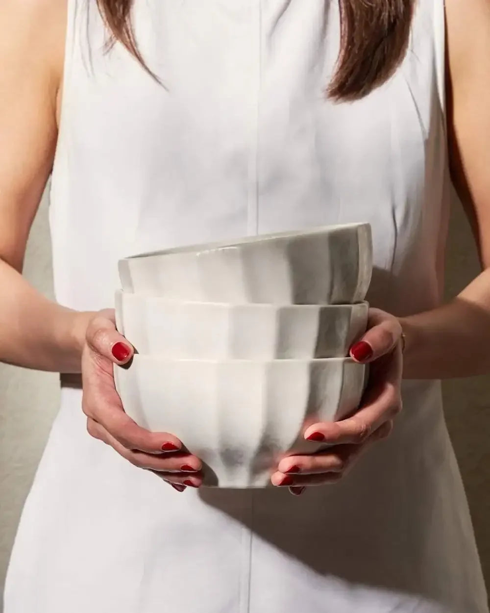 Woman in white holding stacked white ceramic bowls, kitchen homeware essentials