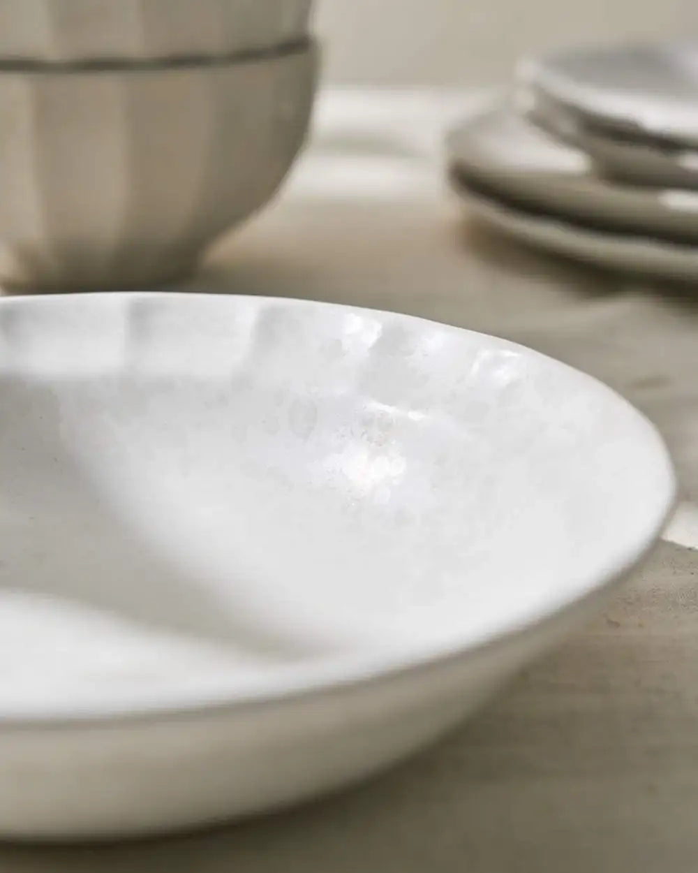Close-up of textured white ceramic bowls and plates set on a neutral fabric surface in a kitchen