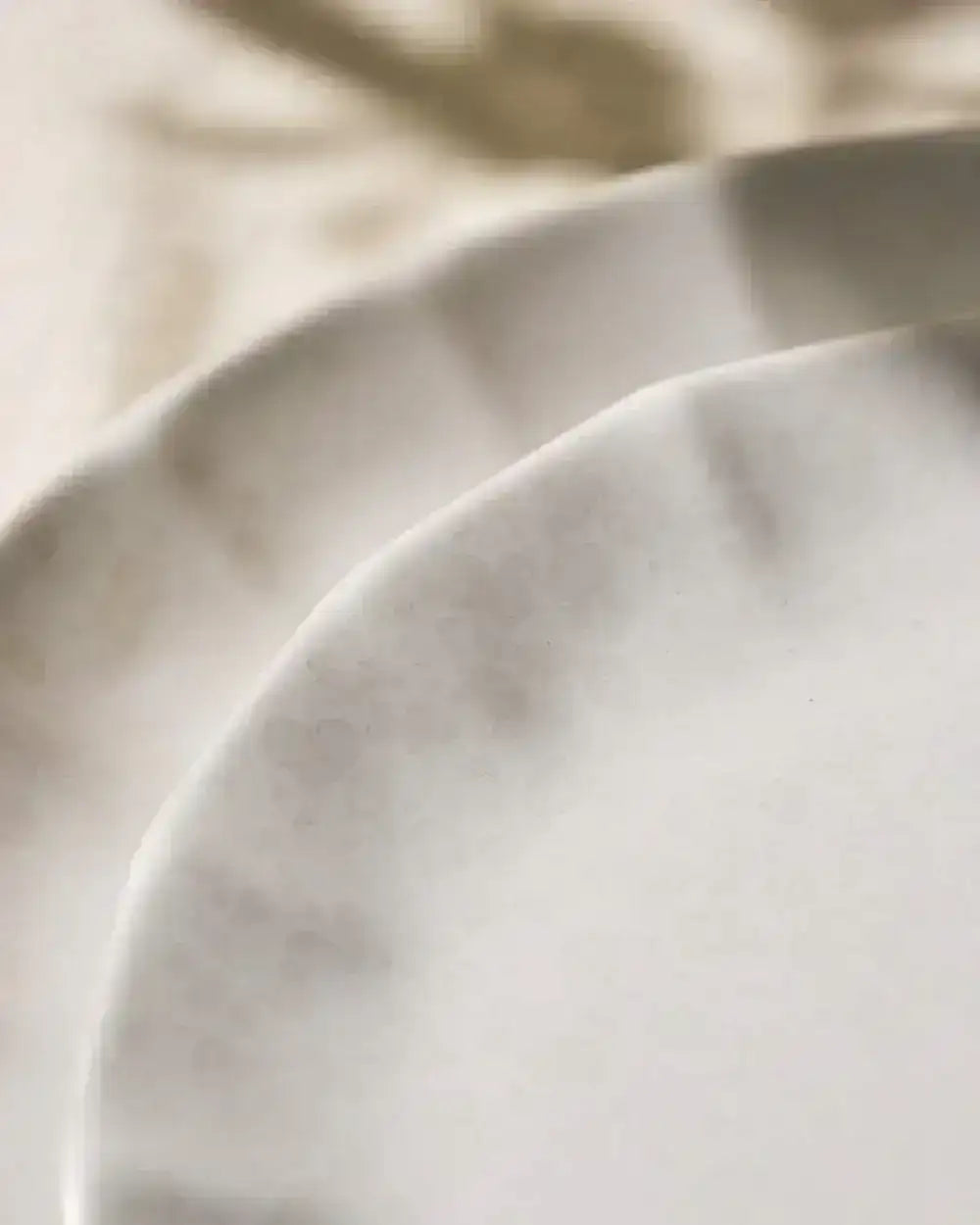 Close-up of textured ceramic plates with beige and white tones showcasing subtle patterns, Asoke kitchenware