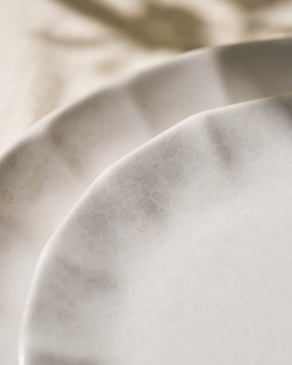 Close-up of two white ceramic plates with subtle textured finish, minimalist tableware