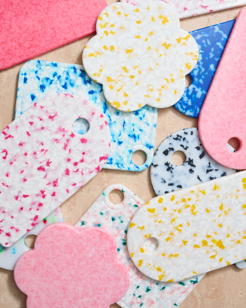 Colorful terrazzo resin cutting boards and coasters in various shapes on a beige surface