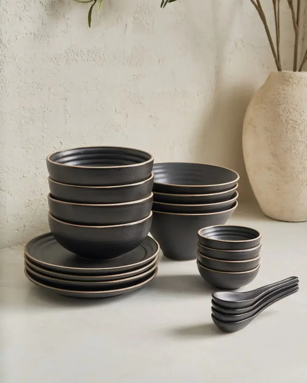 Charcoal ceramic dinnerware set with bowls, plates, and spoons on a light surface