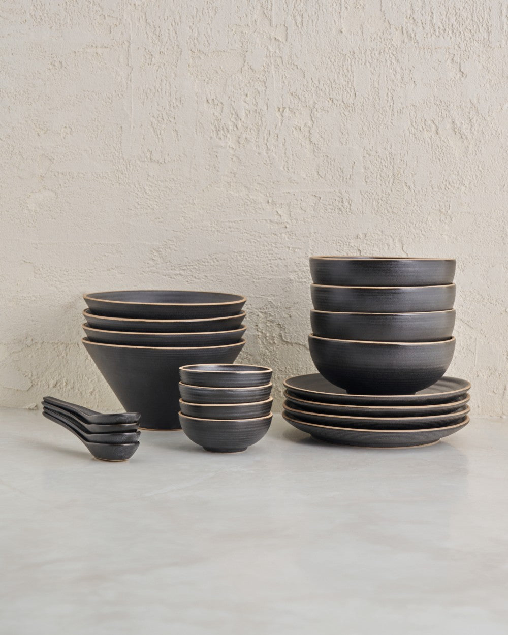Charcoal ceramic noodle bowl set with plates, small bowls, and soup spoons on a light surface