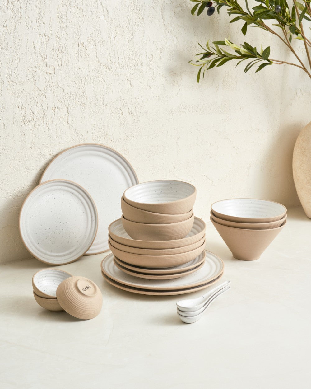 Neutral stoneware dinnerware set with plates, bowls, and spoons on a light table.