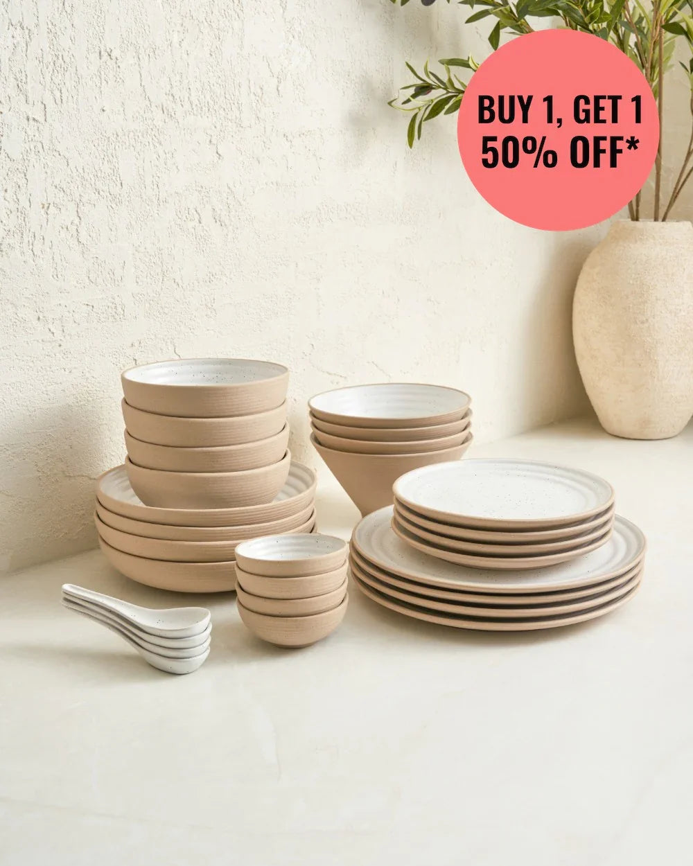 Anaya speckled beige dinnerware set with plates, bowls, and spoons on white surface near textured wall and vase