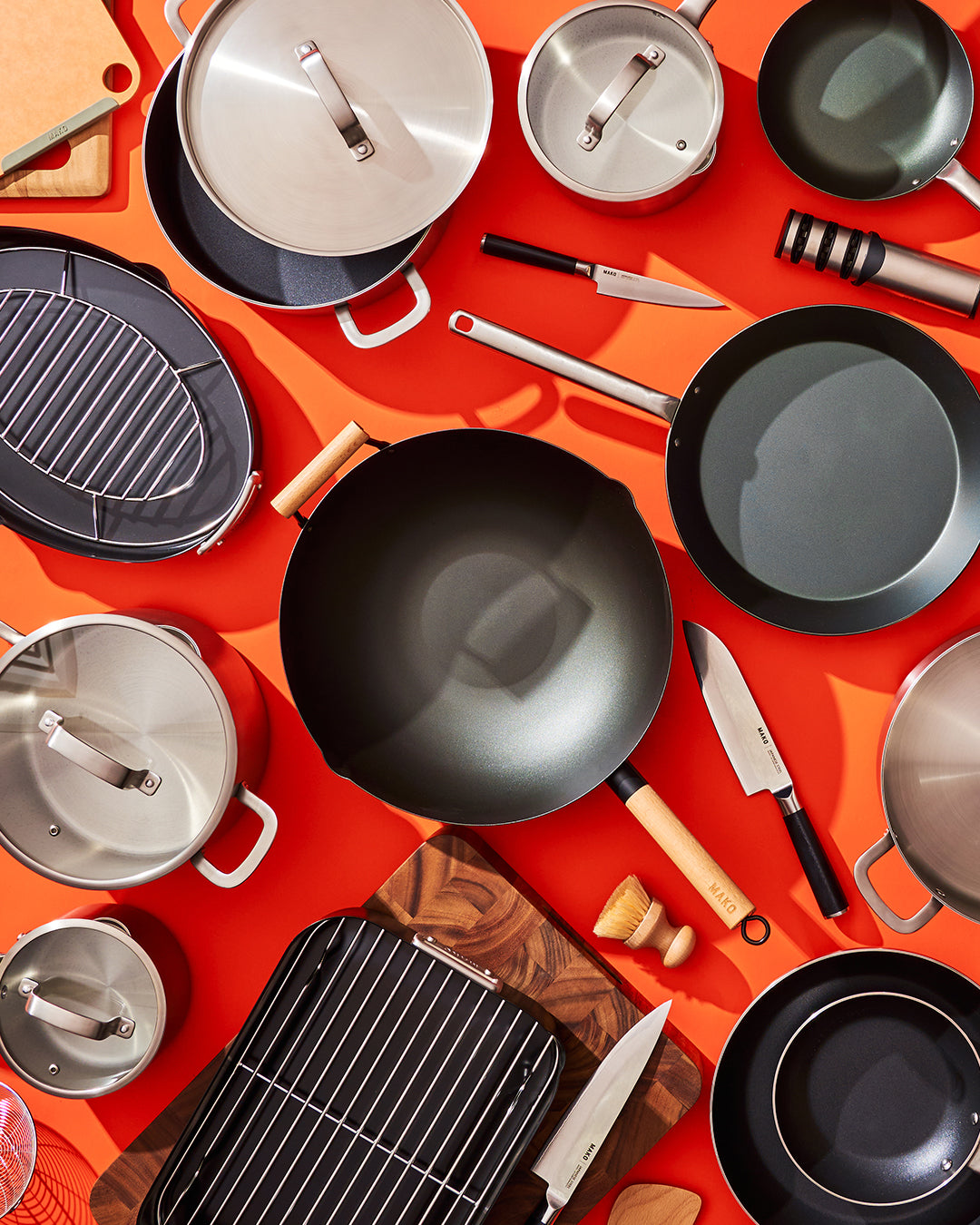 Overhead spread of MAKO cookware and tools on an orange background