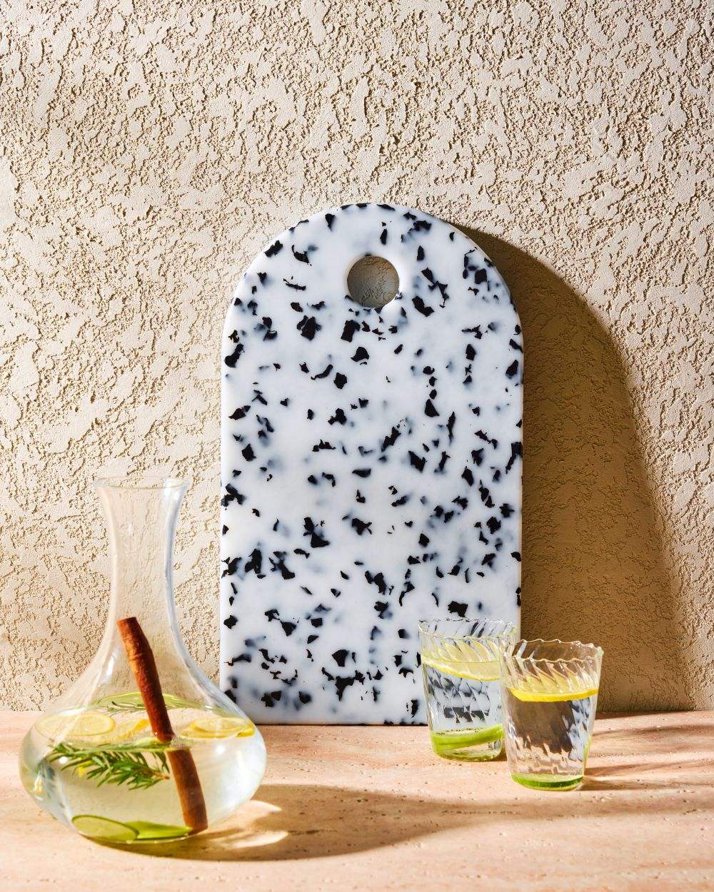 Speckled white and black terrazzo cutting board with clear carafe and glasses of water with lemon