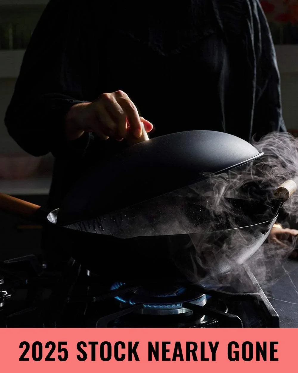 Hand lifting lid off steaming black wok on gas stove in dim kitchen