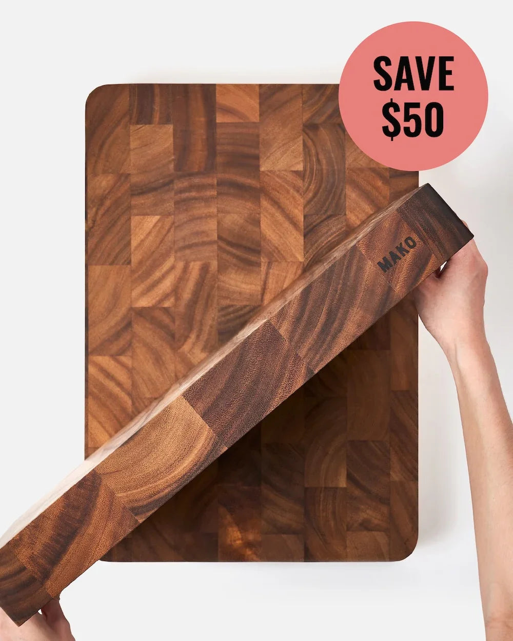 Hands holding thick Mako wood cutting board above matching wooden board with Save $50 label