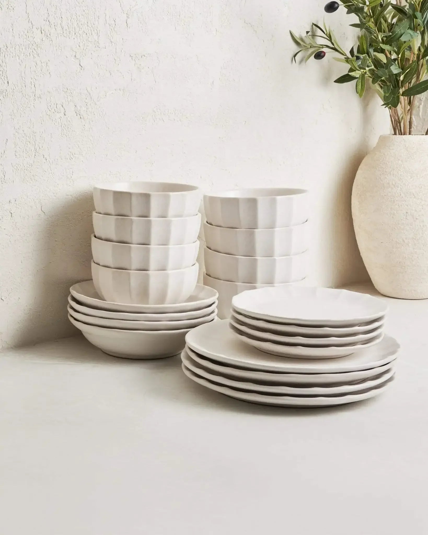 Neutral ceramic dinnerware set with textured bowls and plates on a light countertop