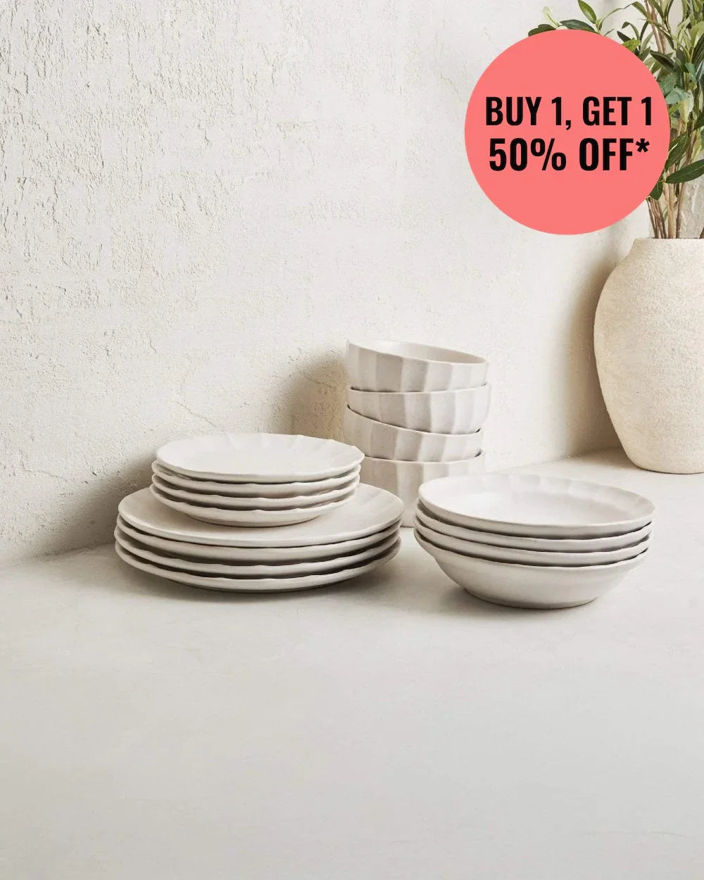 16-piece white dinnerware set with plates and bowls on a light surface, rustic wall, and plant vase