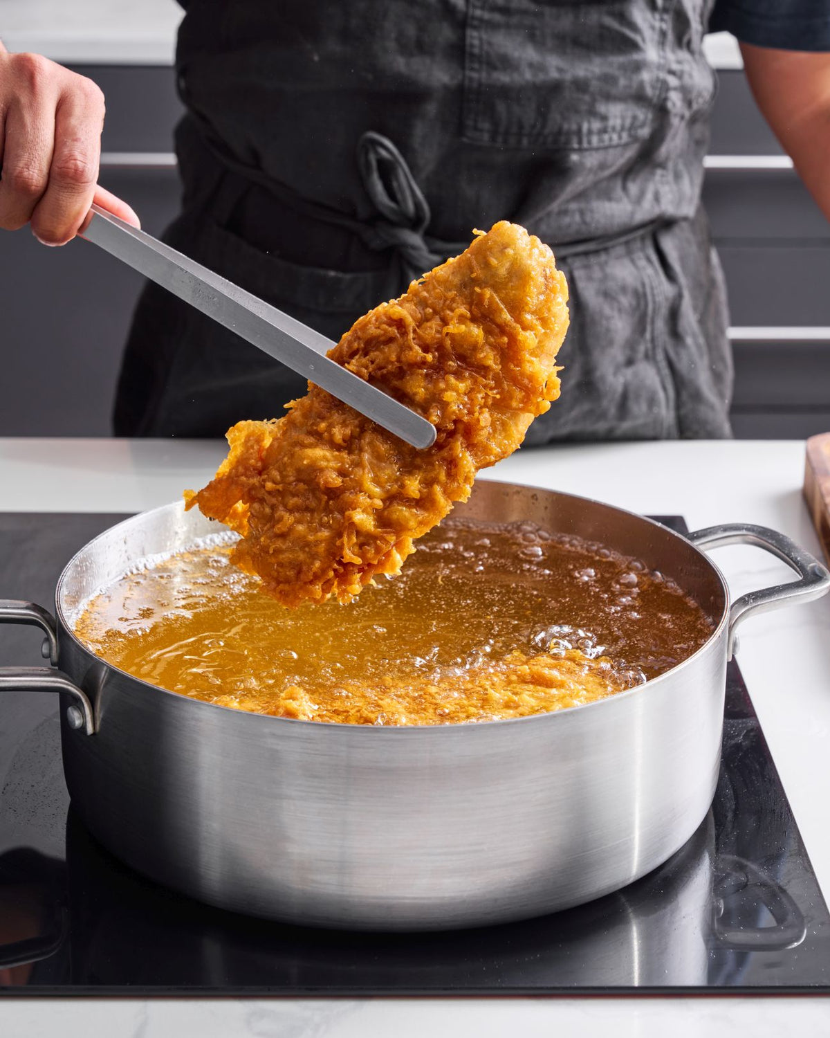 a piece of golden battered fish from a large pot of bubbling hot oil using metal tongs.