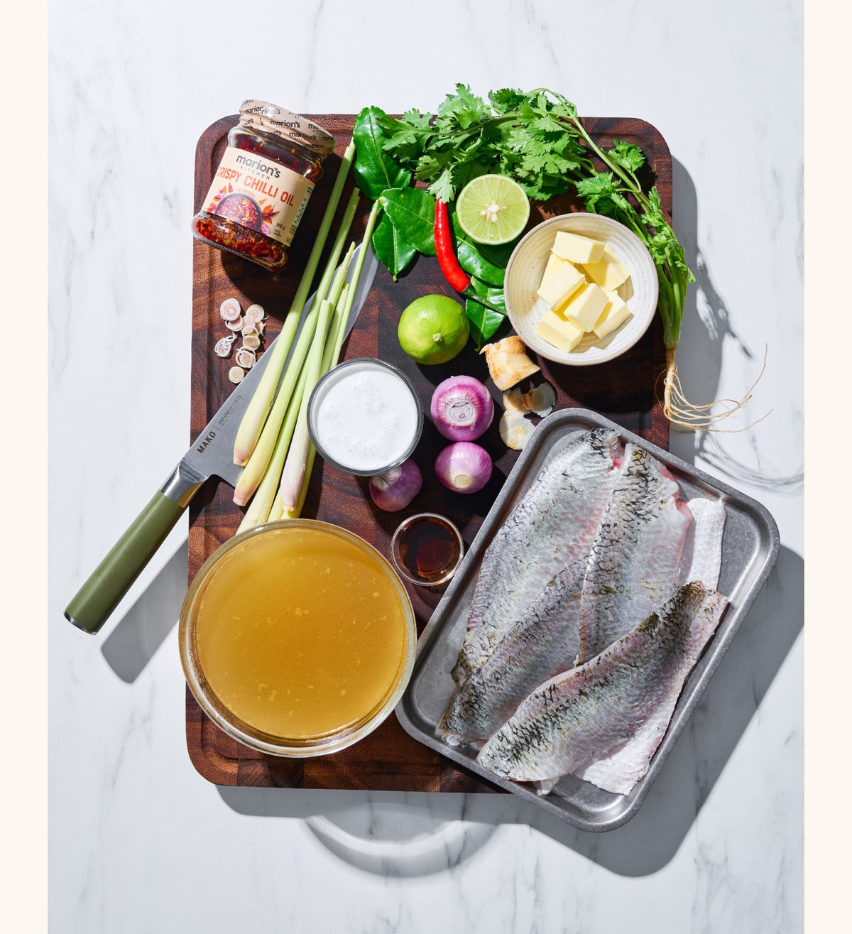 Raw fish on a tray with Marion's Kitchen Crispy Chilli Oil and various other ingredients and condiments on a MAKO wooden board.
