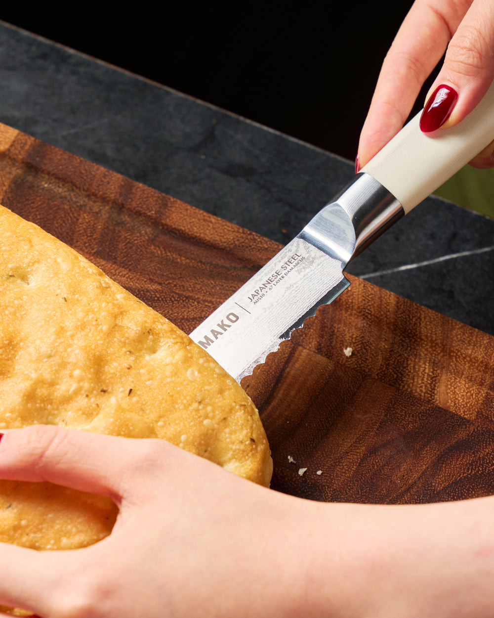 MAKO Japanese Steel Cream 8″ Bread Knife CookDineHost close up in use cutting into bread on wooden chopping board knife blade and handle detail