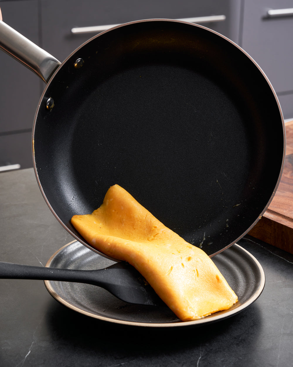 Non-stick frying pan releasing a rolled omelette onto a plate in a modern kitchen