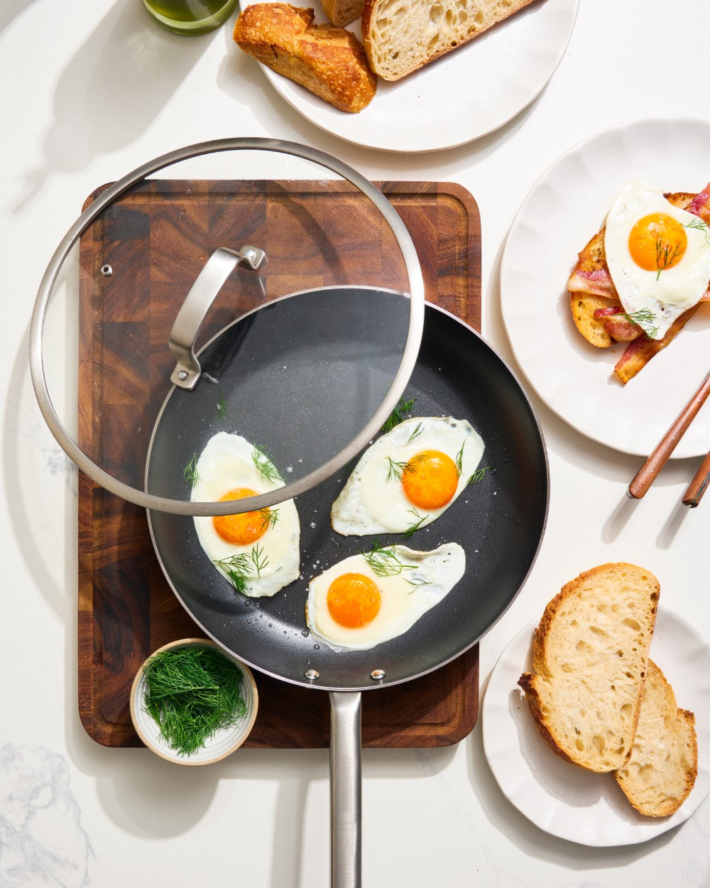 Fried eggs in MAKO non-stick frying pan with toast and herbs on a white surface