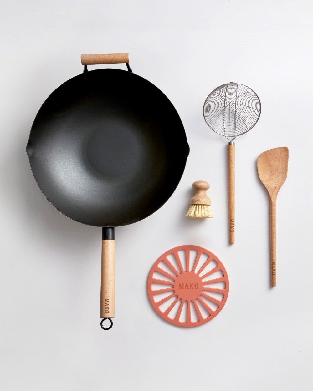 Black steel wok kit with wooden handles, spatula, whisk, cleaning brush, and trivet on white background