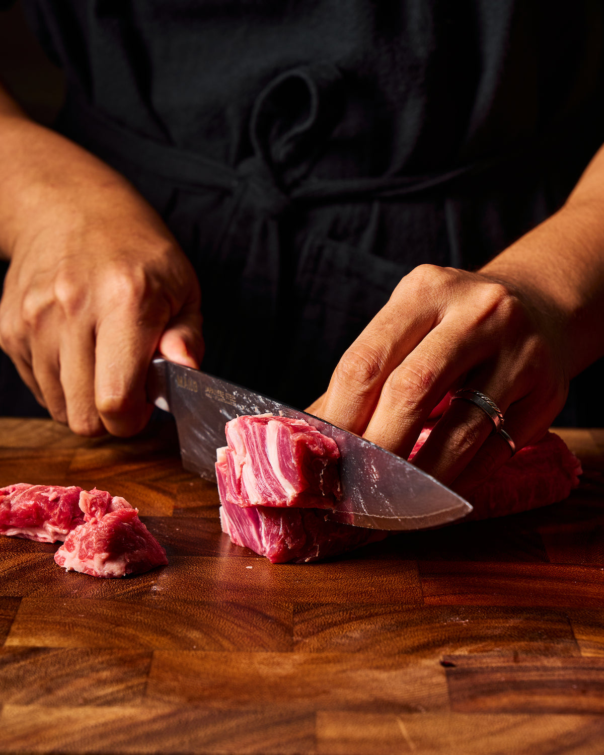 A close-up of a person's hands slicing raw red meat with a MAKO chef knife