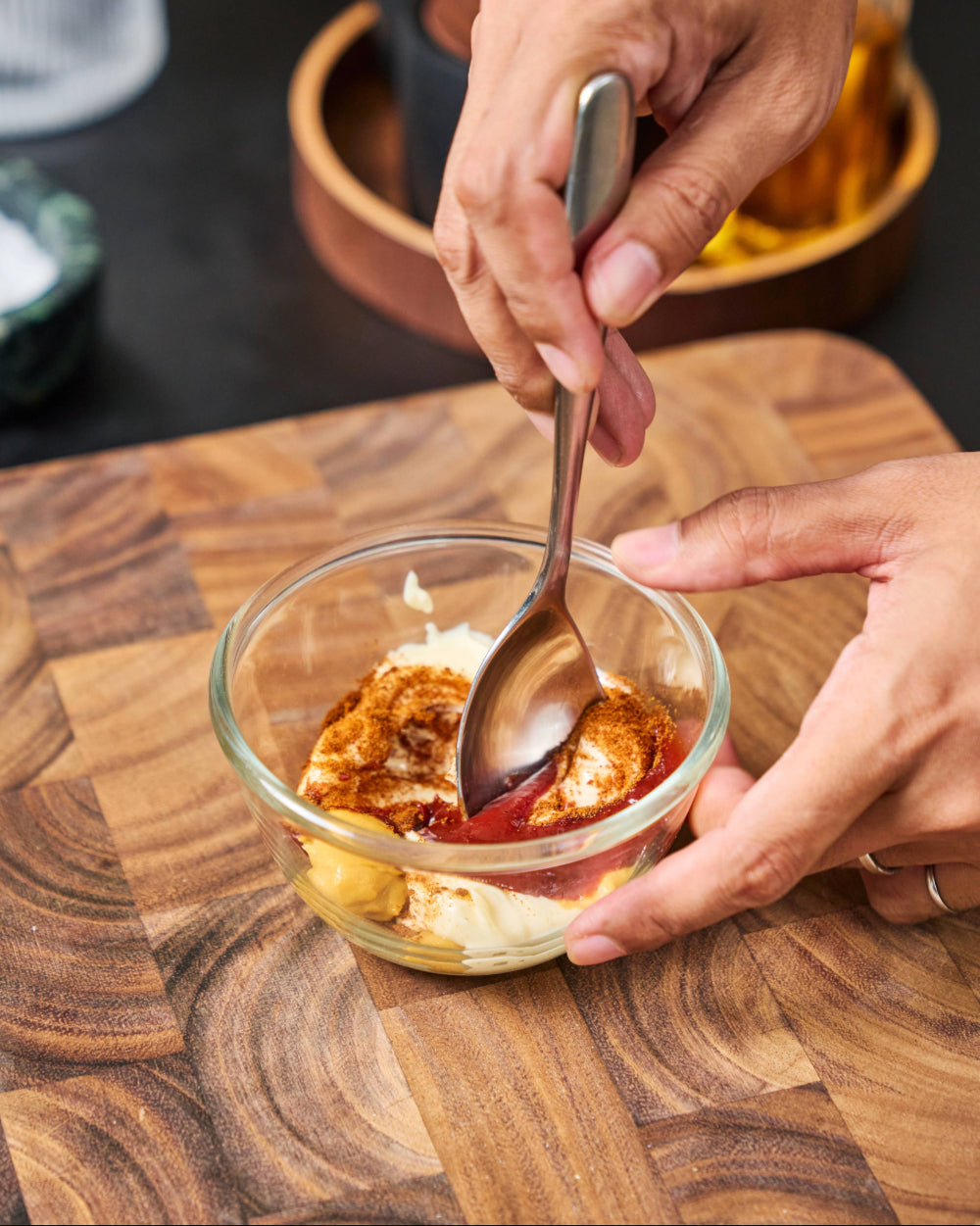 Hands mixing smash burger sauce with mayonnaise, ketchup, mustard and paprika in a small glass bowl on a MAKO wooden chopping board