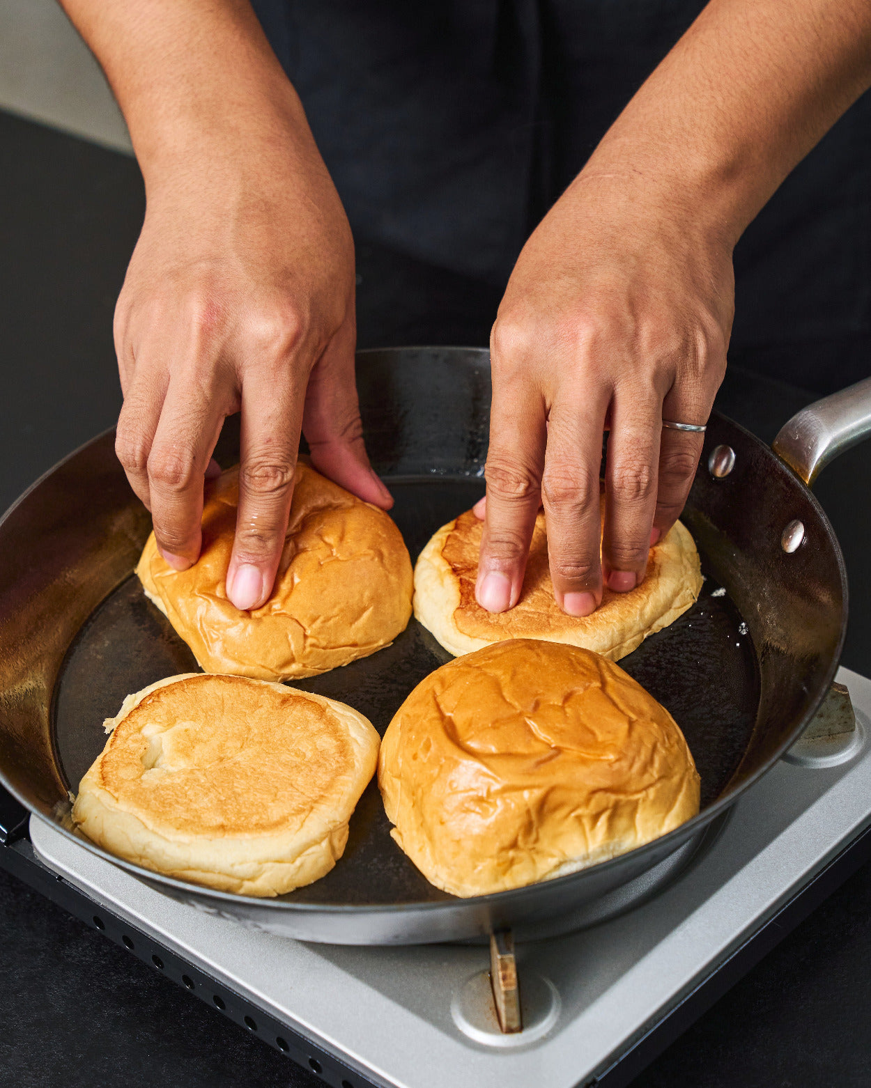 Burger buns being toasted cut-side down in a MAKO carbon steel steak pan on a stovetop